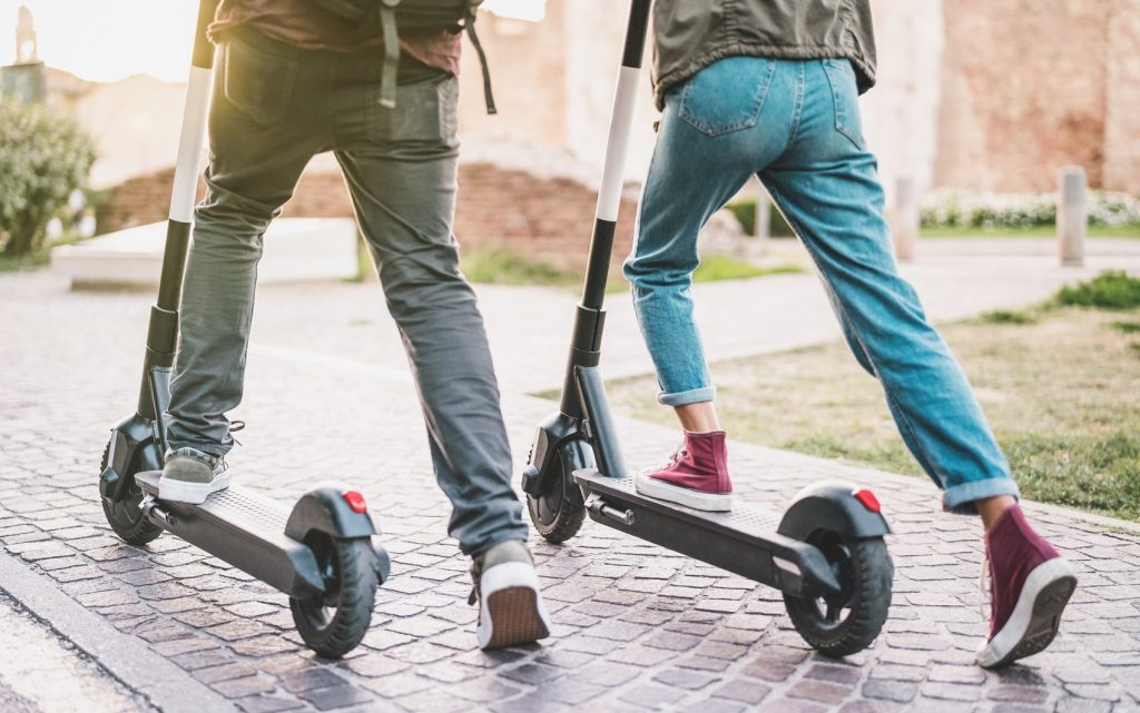 Zwei junge Menschen von hinten, die auf E-Scootern starten.
