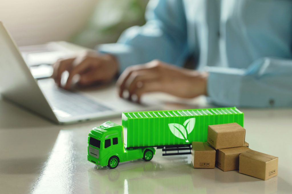 Grüner Modell-LKW steht neben einem Mann, der am Laptop arbeitet.