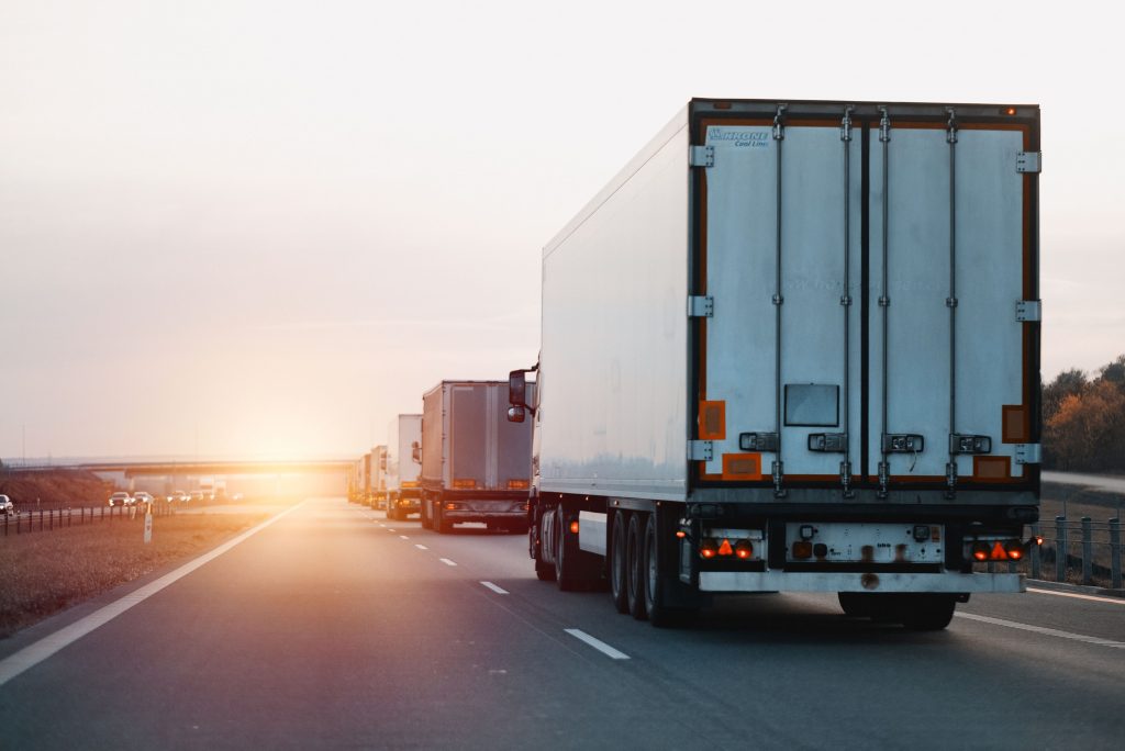 LKWs fahren auf einer Autobahn Richtung Sonnenuntergang.