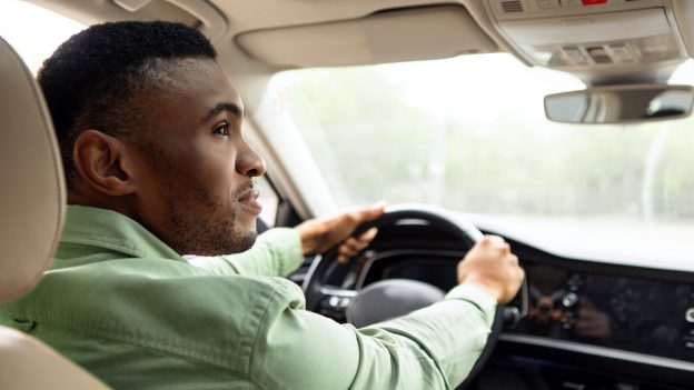 Fahrer sitzt am Steuer eines Autos und blickt zur Seite.