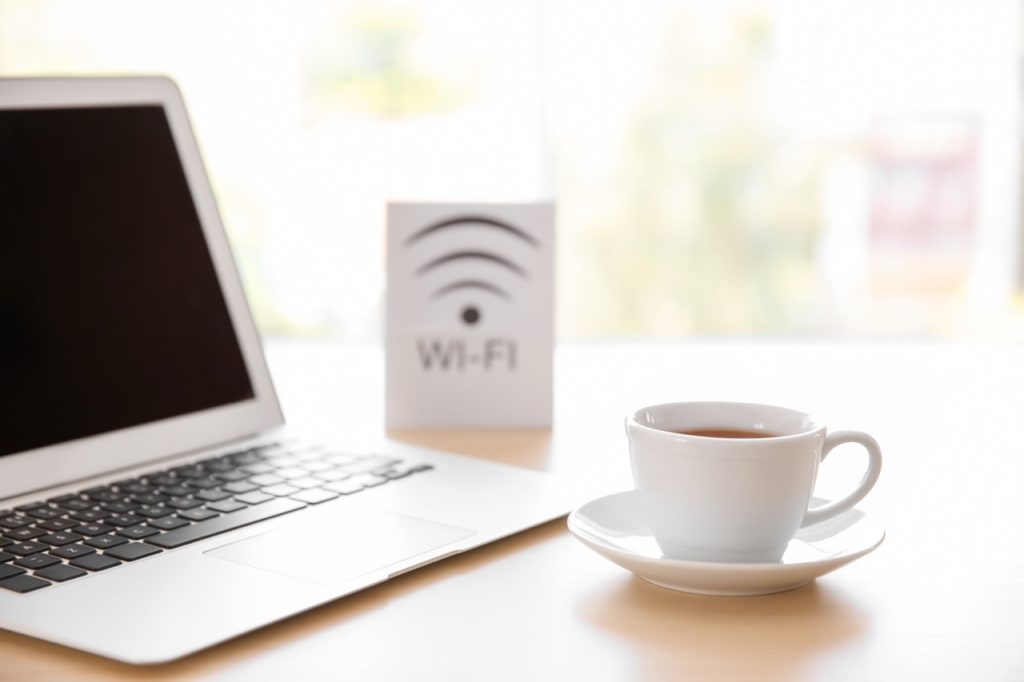 Sicher online unterwegs: Eine Tasse vor einem Laptop und einem "WLAN"-Schild in einem Hotel.