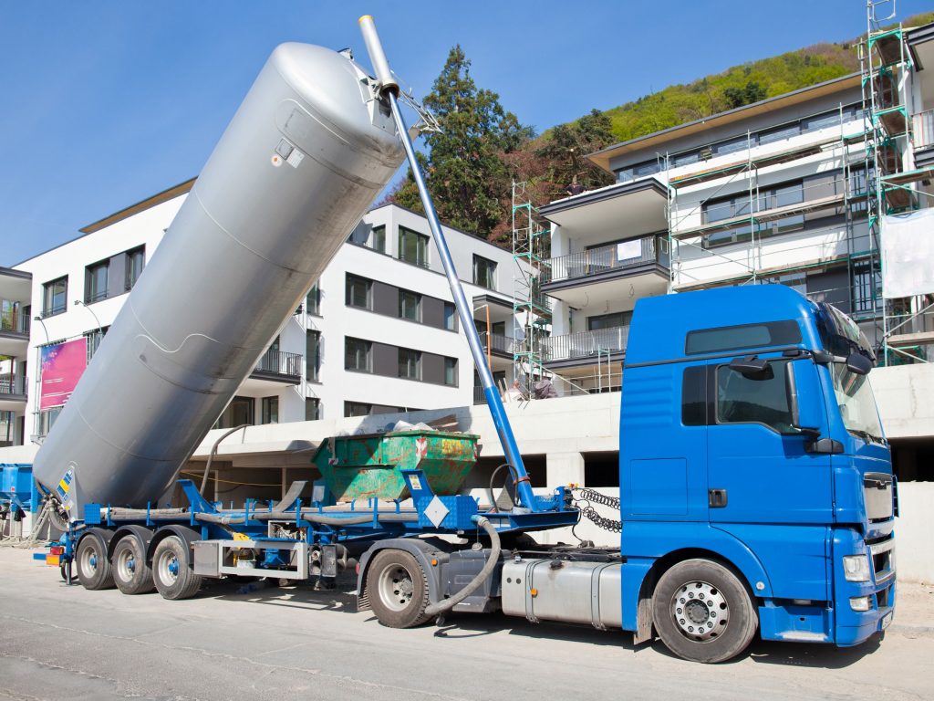 Ein blauer LKW lädt seine Ladung an einer Baustelle mit Mehrfamilienhäusern ab.