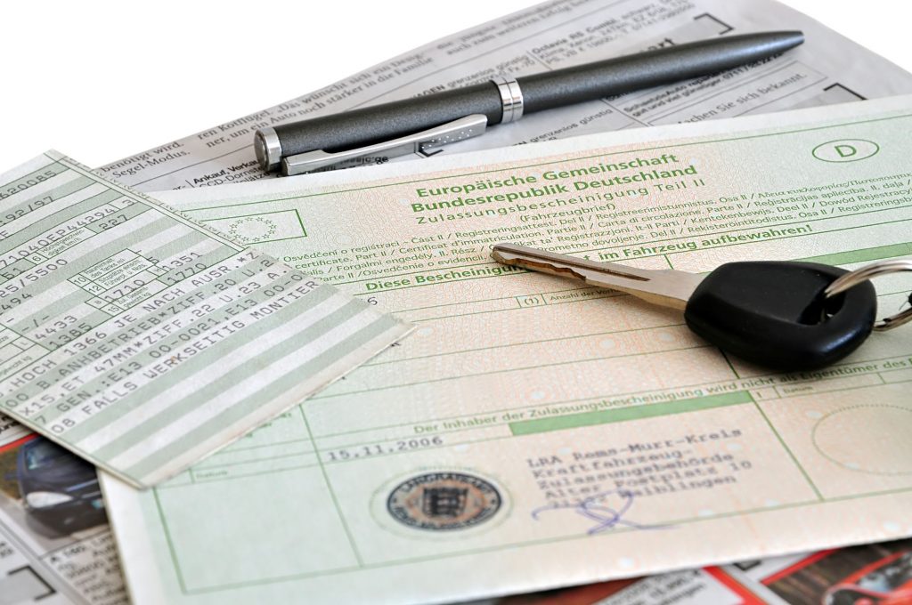 Fahrzeugpapiere, Autoschlüssel und Kugelschreiber liegen auf einer Oberfläche.