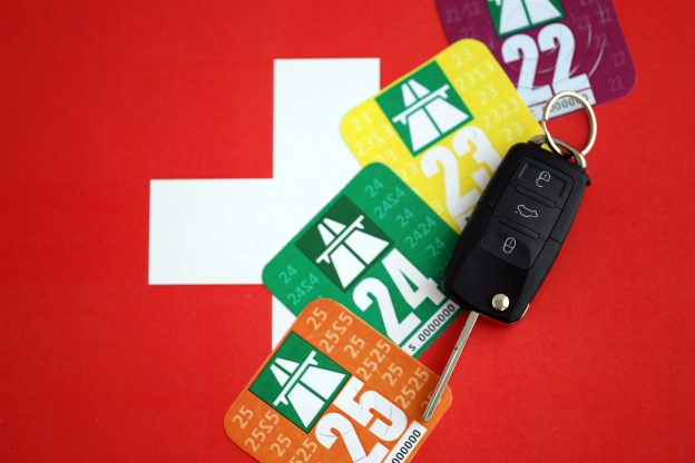 Auf einer schweizer Flagge liegen vier Autovignetten und ein Autoschlüssel.
